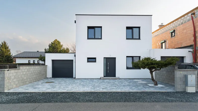 Modernes weißes Einfamilienhaus mit Flachdach, integrierter Garage und gepflasterter Einfahrt.