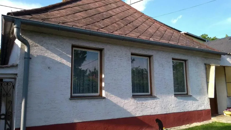 Einfaches Wohnhaus mit Ziegeldach, weißer Fassade und roten Akzenten im Sonnenlicht.