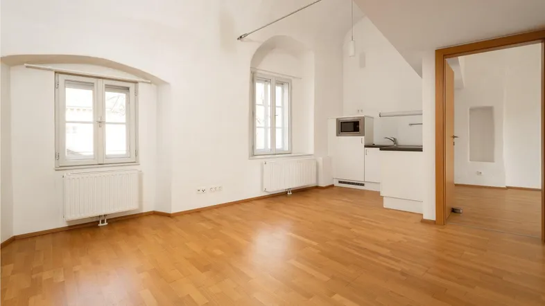 Helles Wohnzimmer mit Parkettboden, hohen Decken und integrierter Küchenzeile.