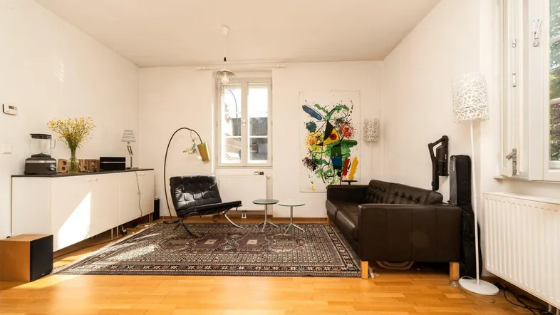 Helles Wohnzimmer mit Parkettboden, bequemen Ledermöbeln und einem farbenfrohen Kunstwerk an der Wand.