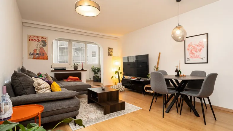 Helles Wohn- und Esszimmer mit Parkettboden, bequemer Couch und modernem Esstisch.