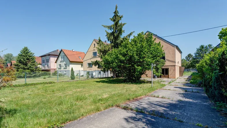 Blick auf das Mehrfamilienhaus mit großem Grundstück und angrenzender Straße an einem sonnigen Tag.