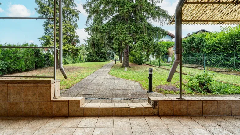 Überdachte Terrasse mit Fliesenboden und Blick auf den grünen Gartenbereich.