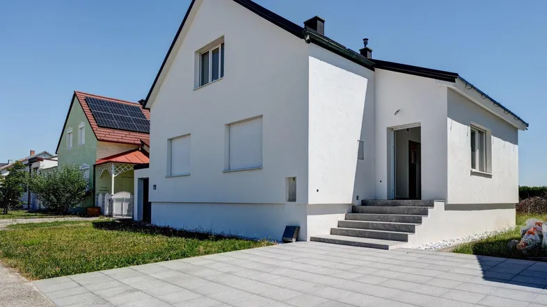 Modernes Einfamilienhaus mit weißer Fassade, schwarzem Dach und gepflasterter Auffahrt.