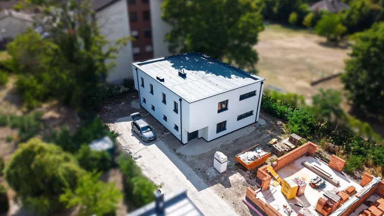 Luftaufnahme eines modernen Neubaus mit Flachdach und angrenzender Baustelle für weitere Gebäude.