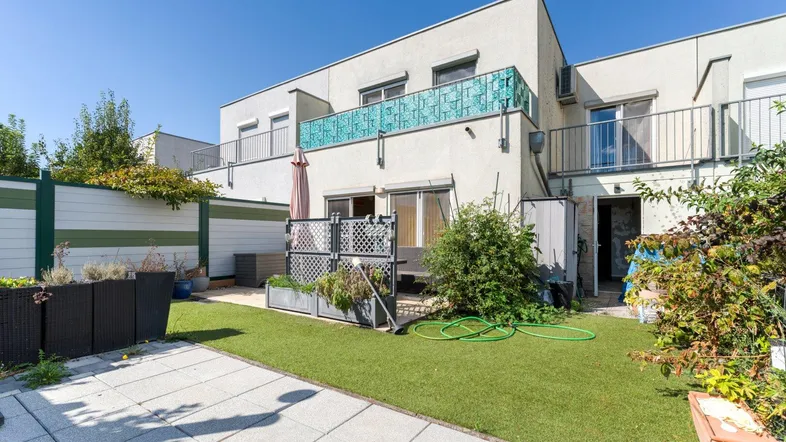 Moderner Gebäudekomplex mit kleinem Gartenbereich, Kunstrasen und gepflasterter Terrasse im Freien.