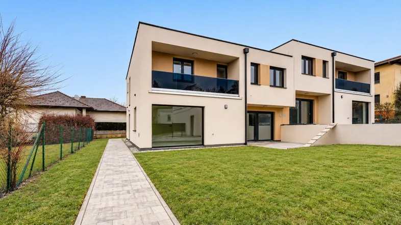 Moderne Reihenhäuser mit beigefarbener Fassade, großen Fenstern und privatem Gartenbereich.