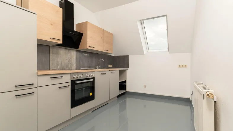 Moderne Einbauküche in Dachgeschosswohnung mit hellgrauen Fronten, Holzakzenten und Dachfenster.