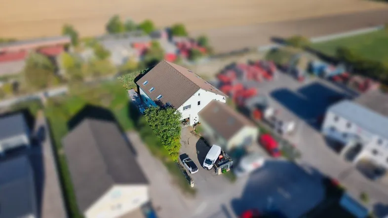 Luftaufnahme eines Gebäudekomplexes mit umliegenden Feldern und einer Zufahrt.