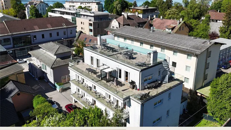 Luftaufnahme eines modernen Gebäudes mit Dachterrassen, umgeben von Natur und Seeblick.