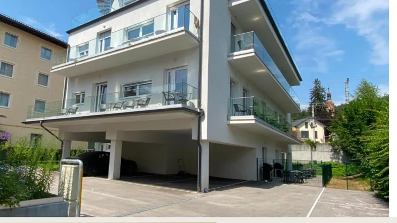 Modernes Mehrfamilienhaus mit mehreren Balkonen und überdachten Parkplätzen im Freien.