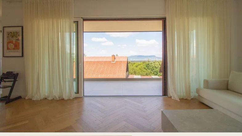 Helles Wohnzimmer mit Fischgrätparkett und Zugang zu einer großen Terrasse mit Weitblick.