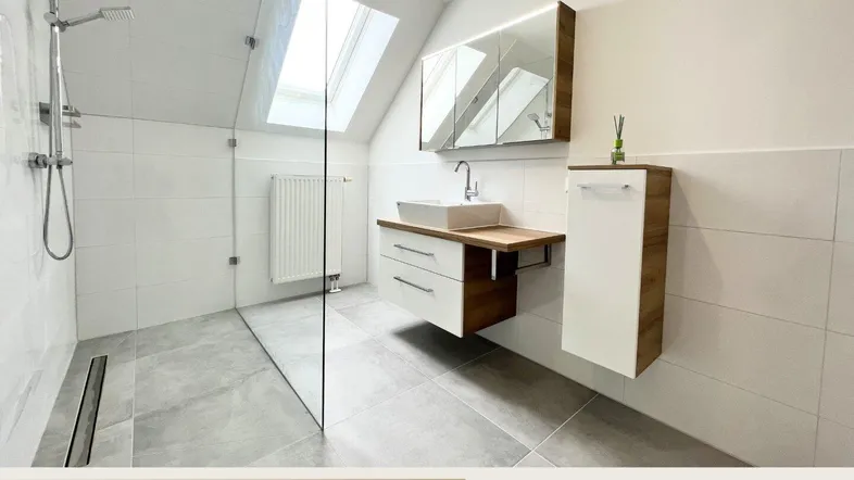 Modernes Badezimmer mit begehbarer Dusche, Waschtisch und Dachfenster, hell gefliest.
