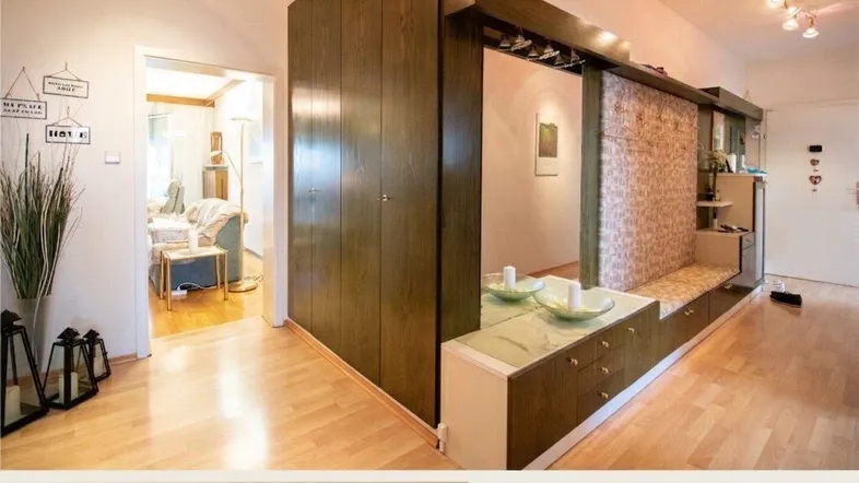Heller Eingangsbereich mit integriertem Garderobenschrank, Spiegel und Holzboden, der in ein gemütliches Wohnzimmer führt.