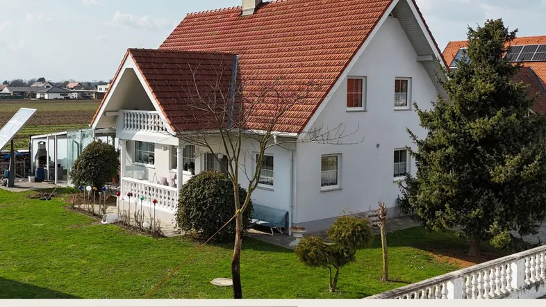 Haus mit rotem Ziegeldach, weißer Fassade und gepflegtem Vorgarten in ländlicher Umgebung.