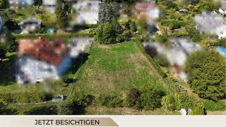 Luftaufnahme eines unbebauten Grundstücks mit grüner Wiese, umgeben von Bäumen und Häusern.
