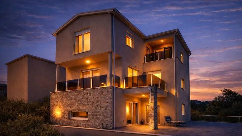 Moderne Villa mit mehreren Balkonen und Steinfassade, beleuchtet bei Sonnenuntergang.