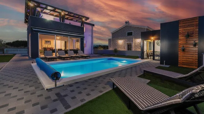 Moderne Villa mit beleuchtetem Pool und Liegebereich unter einem dramatischen Sonnenuntergangshimmel.