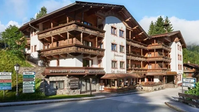 Traditionelles alpines Gebäude mit vielen Holzbalkonen und einer steinernen Basis, umgeben von Bergen.