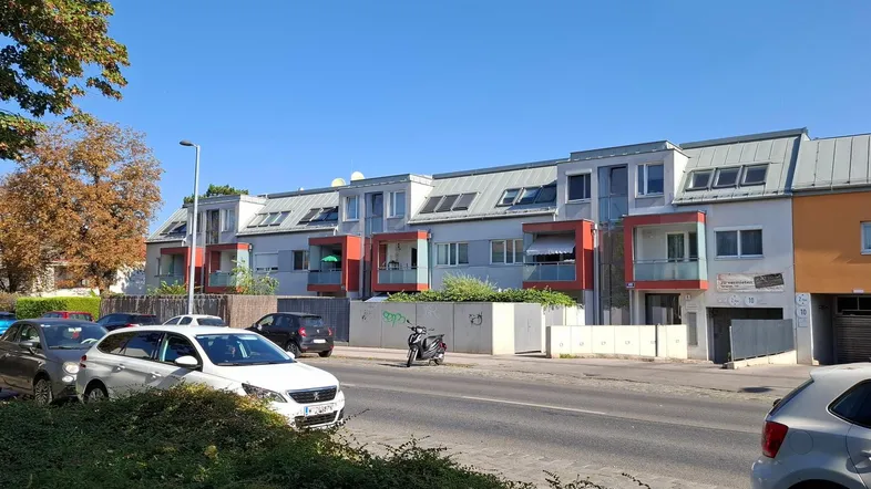 Moderne Reihenhäuser mit orangefarbenen Akzenten und Schrägdächern entlang einer ruhigen Wohnstraße.