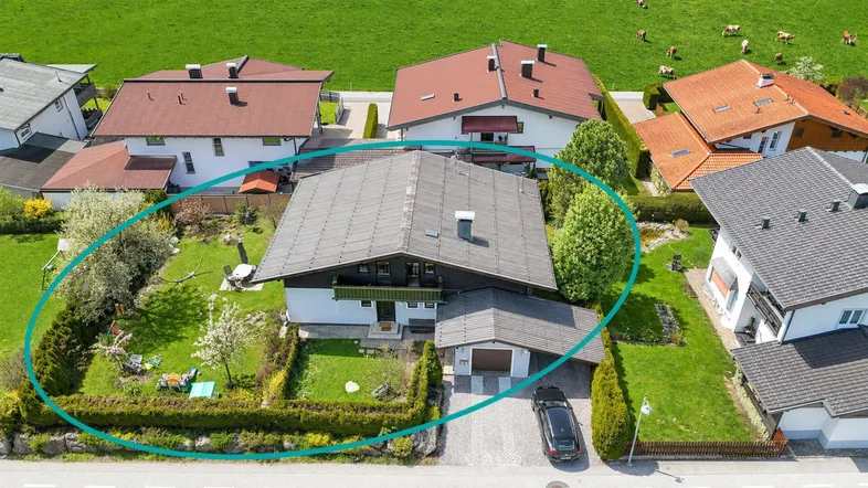 Luftaufnahme eines Hauses mit Garten und umliegender grüner Landschaft, umrandet von einem Kreis.