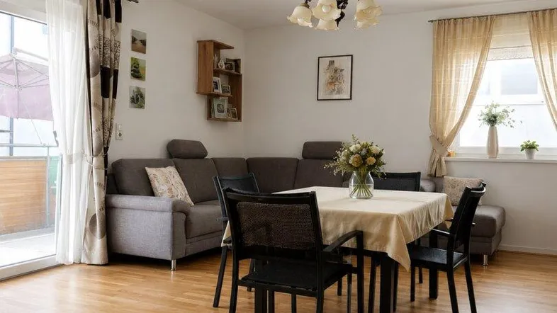 Heller Wohn-Essbereich mit Holzboden, Esstisch und Zugang zu einem Balkon.