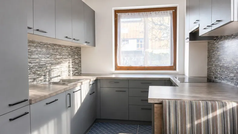 Moderne Küche mit grauen Schränken, Steinoptik-Rückwand, integrierter Sitzecke und Fenster für natürliches Licht.