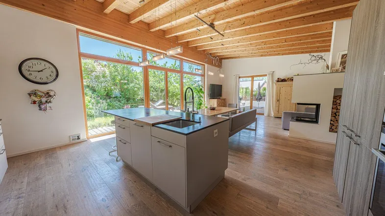 Moderne offene Küche mit Kochinsel, Holzbalkendecke und Blick in den Garten.