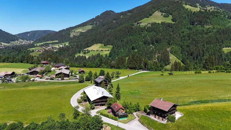 Panoramablick auf eine idyllische Berglandschaft mit traditionellen Häusern und grünen Wiesen unter blauem Himmel.