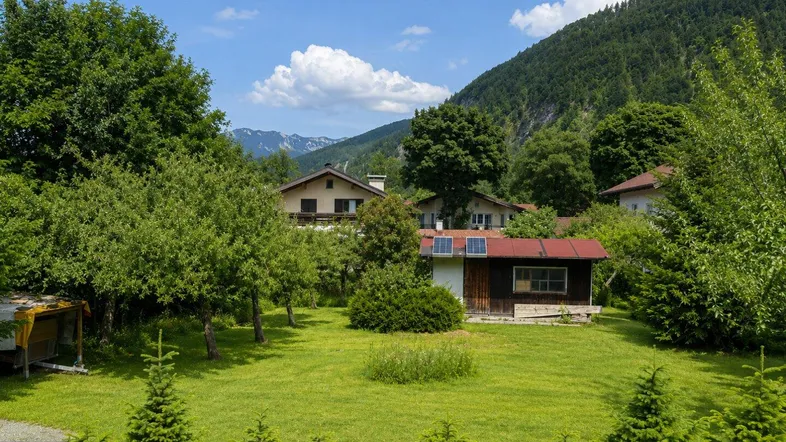 Großer grüner Garten mit Rasenfläche, Bäumen und einem kleinen Schuppen mit Solarpaneelen.