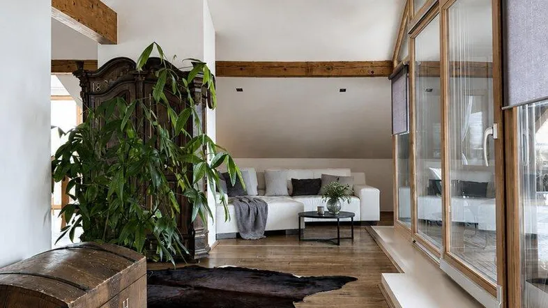 Geräumiges Wohnzimmer mit Holzbalken, Parkettboden und großen Fenstern, die viel Tageslicht hereinlassen.
