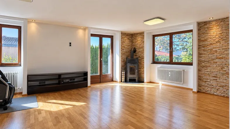 Geräumiges Wohnzimmer mit Holzboden, Kaminofen und Zugang zum Garten, umgeben von natürlichem Licht.