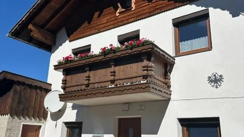 Traditionelles Haus mit Holzbalkon, dekorativen Elementen und Rollläden an den Fenstern.