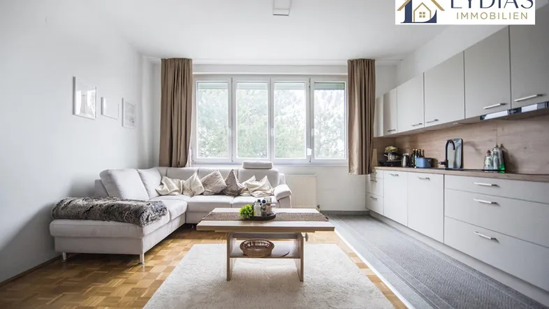 Helles Wohnzimmer mit integrierter Küche, Parkettboden und großem Fenster mit Blick ins Grüne.