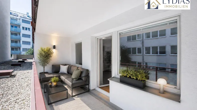 Möblierter Balkon mit gemütlichem Sitzbereich und Blick auf die umliegenden Gebäude.