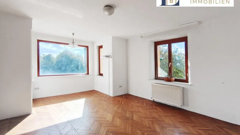 Helles Zimmer mit Fischgrätparkett und großen Fenstern, bereit zur individuellen Gestaltung.