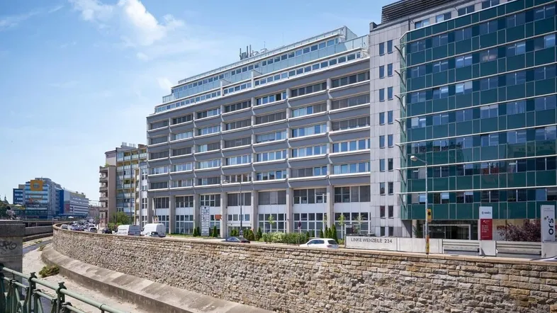 Modernes Bürogebäude mit gestufter Fassade, großen Fenstern und Außenjalousien in städtischer Umgebung.