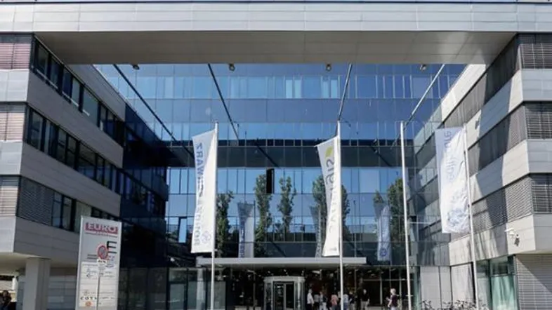 Modernes Bürogebäude mit großer Glasfassade und Eingangsbereich, umgeben von Fahnen und Fahrrädern.