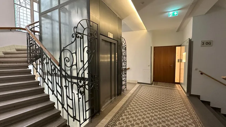 Treppenhaus und Flur mit historischem Fliesenboden und Aufzug in einem Altbau.