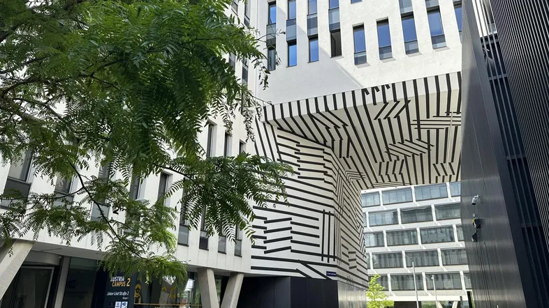 Moderne Bürogebäude mit auffälliger schwarz-weiß gestreifter Fassade und Bäumen im Vordergrund, belebte Straße.