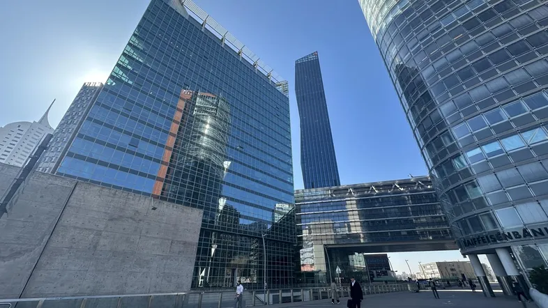 Moderne Glasfassaden von Bürogebäuden unter blauem Himmel mit Menschen auf dem Vorplatz.