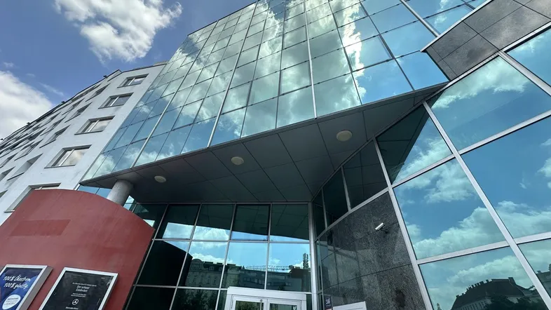 Modernes Bürogebäude mit großer Glasfassade und reflektierendem Himmel, zeigt den Eingangsbereich.