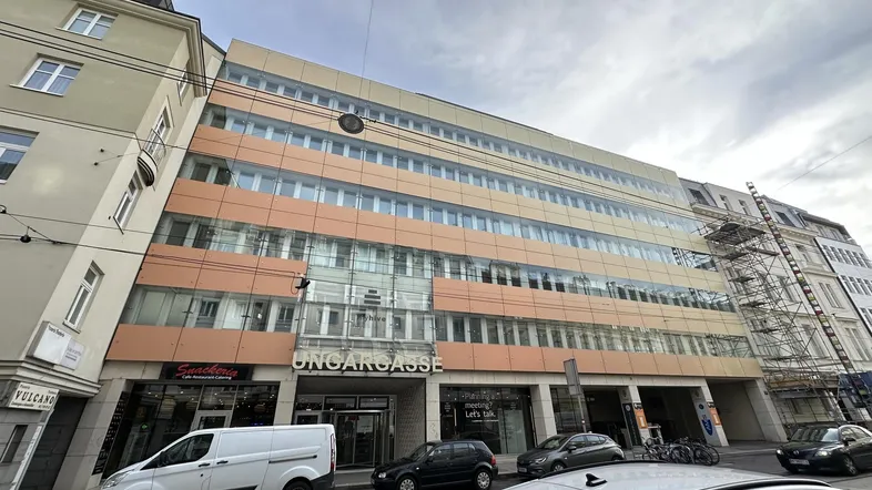 Modernes Bürogebäude mit Glasfassade und orangefarbenen Akzenten an einer belebten Straße.