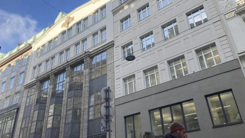 Historisches Gebäude mit markanter Fassade und großen Fenstern in einer belebten Stadtstraße.