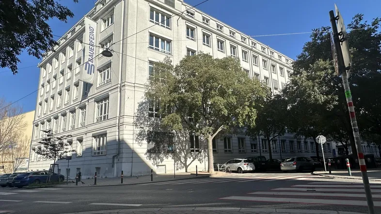 Großes Bürogebäude mit vielen Fenstern und einem Firmenbanner an der Fassade, umgeben von Bäumen.