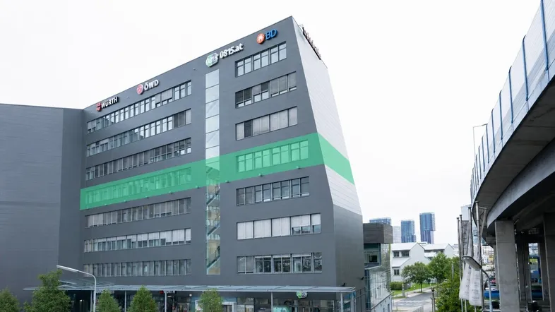 Modernes Bürogebäude mit markanter Architektur und großen Fensterfronten, teilweise grün hervorgehoben.