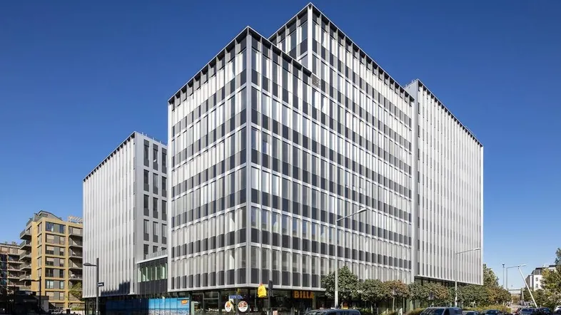 Modernes Bürogebäude mit markanter Glasfassade und vertikalen Lamellen unter blauem Himmel.
