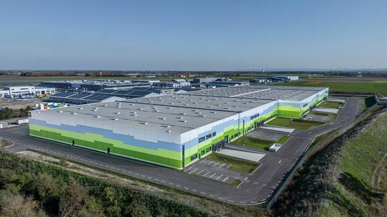 Drohnenaufnahme eines großen, modernen Logistikzentrums mit farbiger Fassade und weitem Blick über die Landschaft.