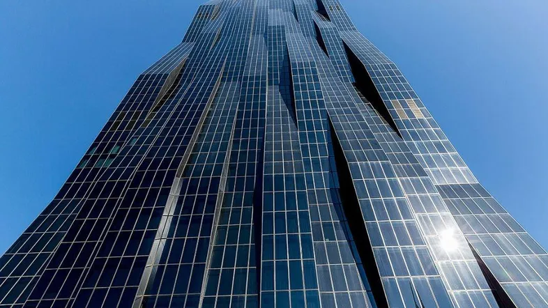 Ein imposantes, modernes Hochhaus mit einer markanten Glasfassade, das sich elegant in den blauen Himmel erhebt.