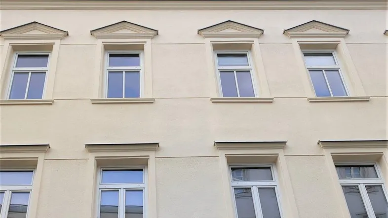 Klassische Fassade eines Altbaus mit vielen Fenstern und dekorativen Elementen im oberen Bereich.